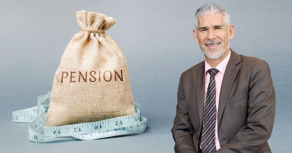 señor de cabello cano y barba, con traje café y camisa rosada, junto a costal con la palabra Pensión