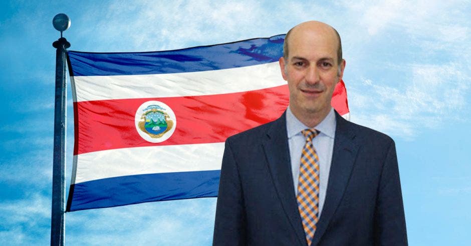 Hombre de traje y corbata frente a bandera de Costa Rica