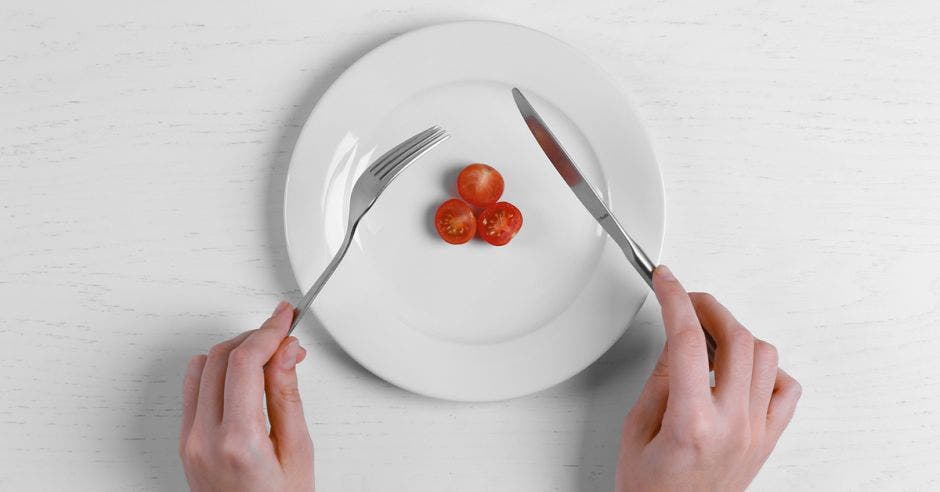 un plato con tres tomates y las manos de una joven sosteniendo cubiertos