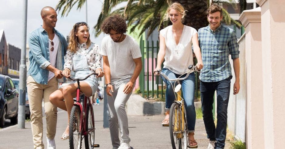 Un grupo de cinco muchachos, dos caminando, dos en bici y uno en patineta en la acera