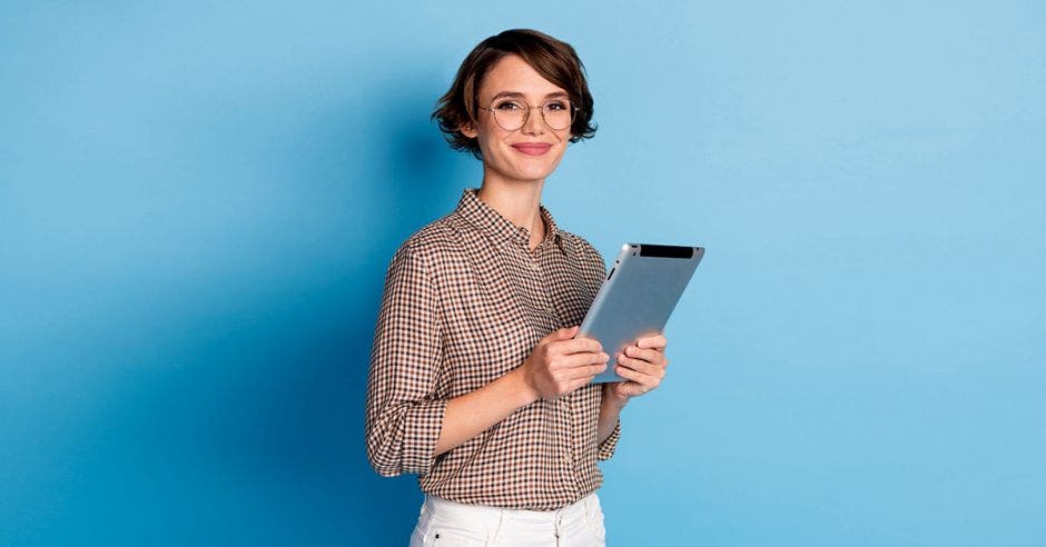 Mujer con una tablet en sus manos y con fondo de pared celeste