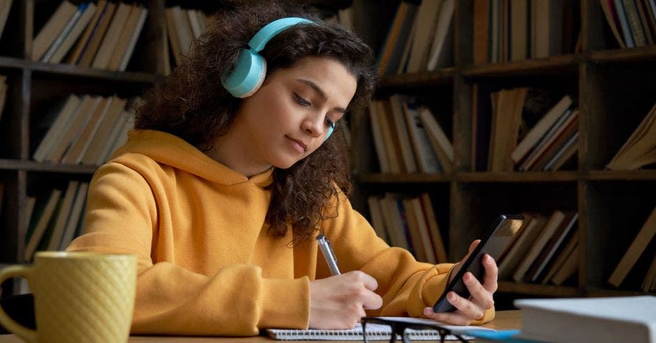 Joven frente a una computadora escribiendo en un cuaderno