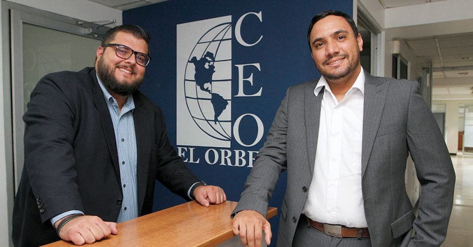 Hombres posando y al fondo letras de la empresa El Orbe