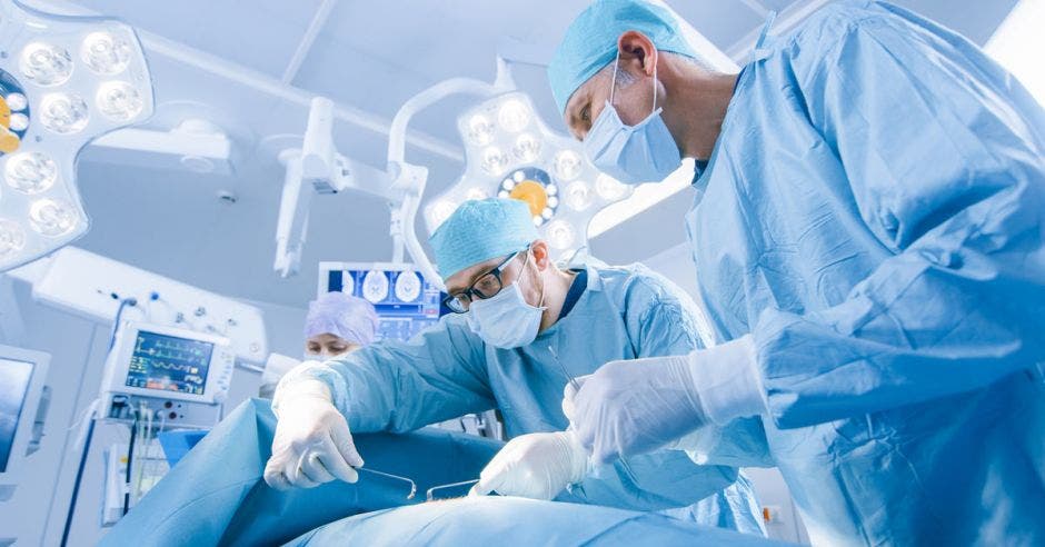 Médicos con trajes celestes realizando un procedimiento médico en una sala de operaciones