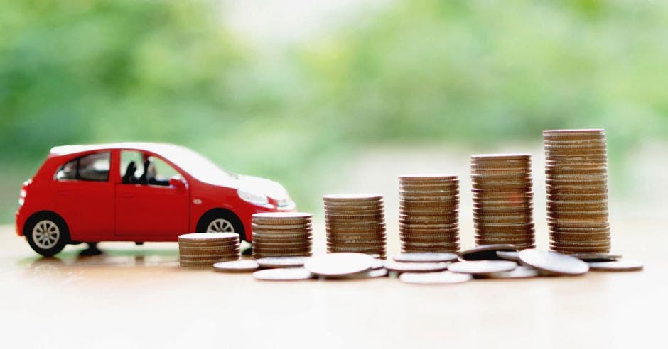 auto rojo miniatura junto a torres de monedas de diferentes tamaños