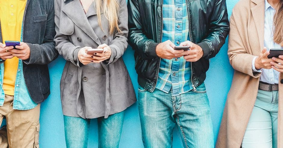 Cuatro personas recostadas a una pared enviando mensajes por teléfono celular