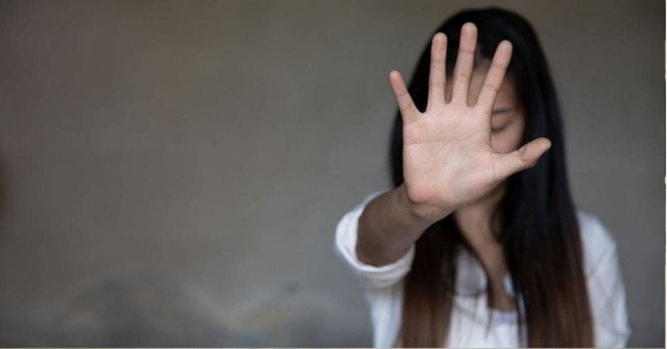 mujer de cabello liso castaño, con mano levantada hacia el frente