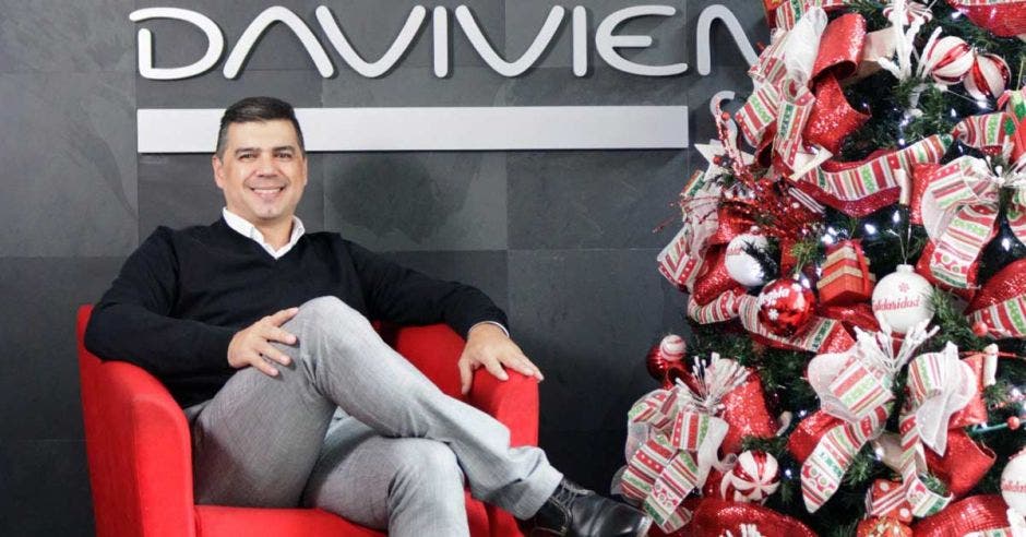 Hombre sentado en un sillón rojo a la par de un árbol de navidad y letras de DAVIVIENDA al fondo