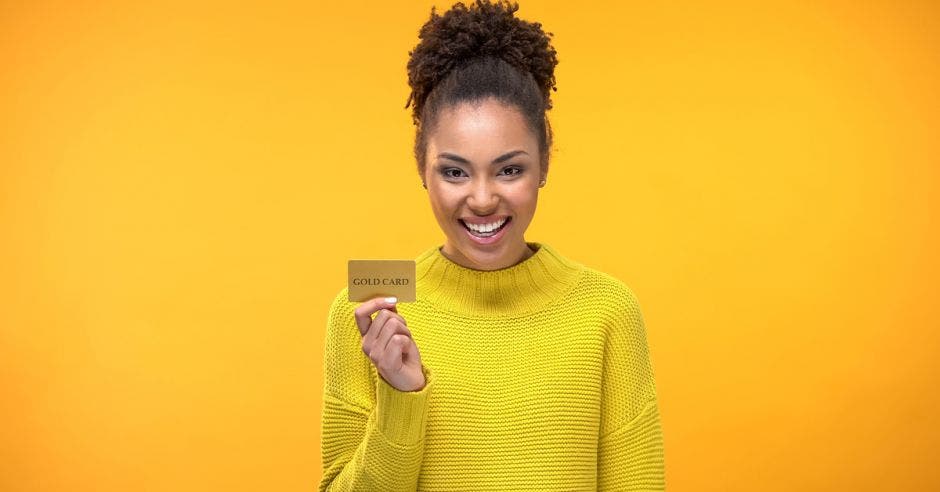 mujer joven con sueter amarillo sosteniendo tarjeta de crédito