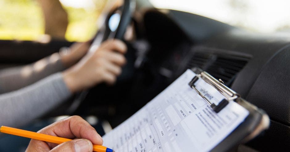 Una persona con una hoja de test al lado de una persona al volante