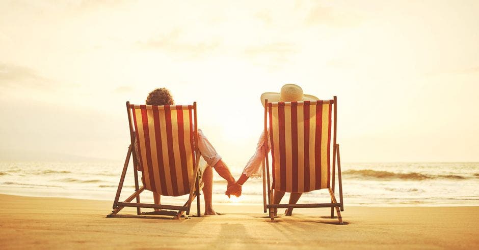 Una pareja de adultos mayores tomada de la manos en una playa