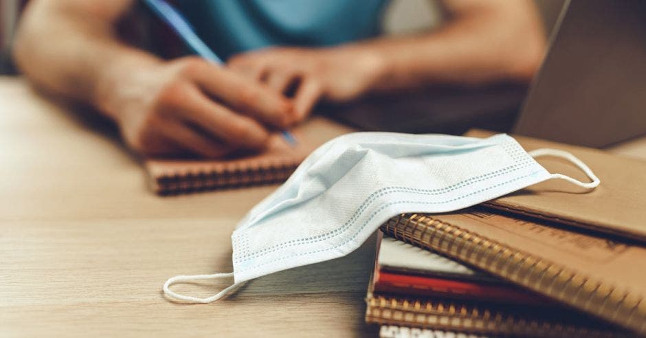 persona estudiando y a la par una mascarilla