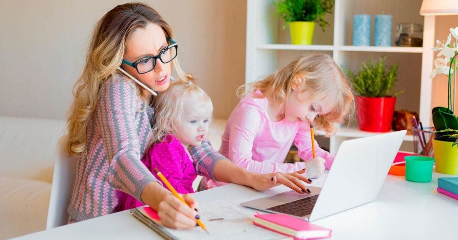 Mamá trabajando en casa con su computadora y alrededor cuidando a sus hijos