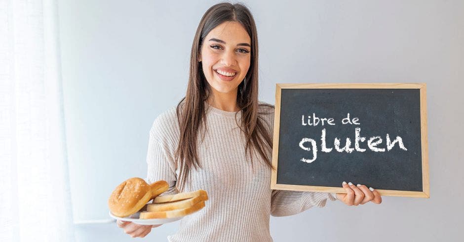 mujer joven celíaca sosteniendo plato con pan y un letrero con el texto "libre de gluten"