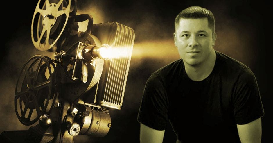Una cámara de cine, al lado un hombre posando con camisa negra.