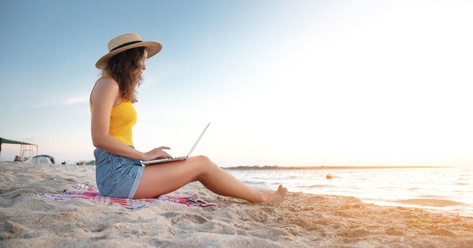 mujer trabajando desde la playa nómadas digitales, teletrabajo